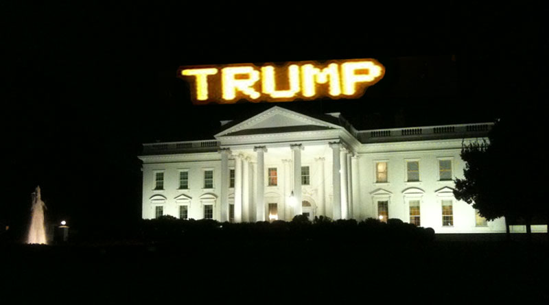 The White House in night against a dark sky with a bright TRUMP sign on top